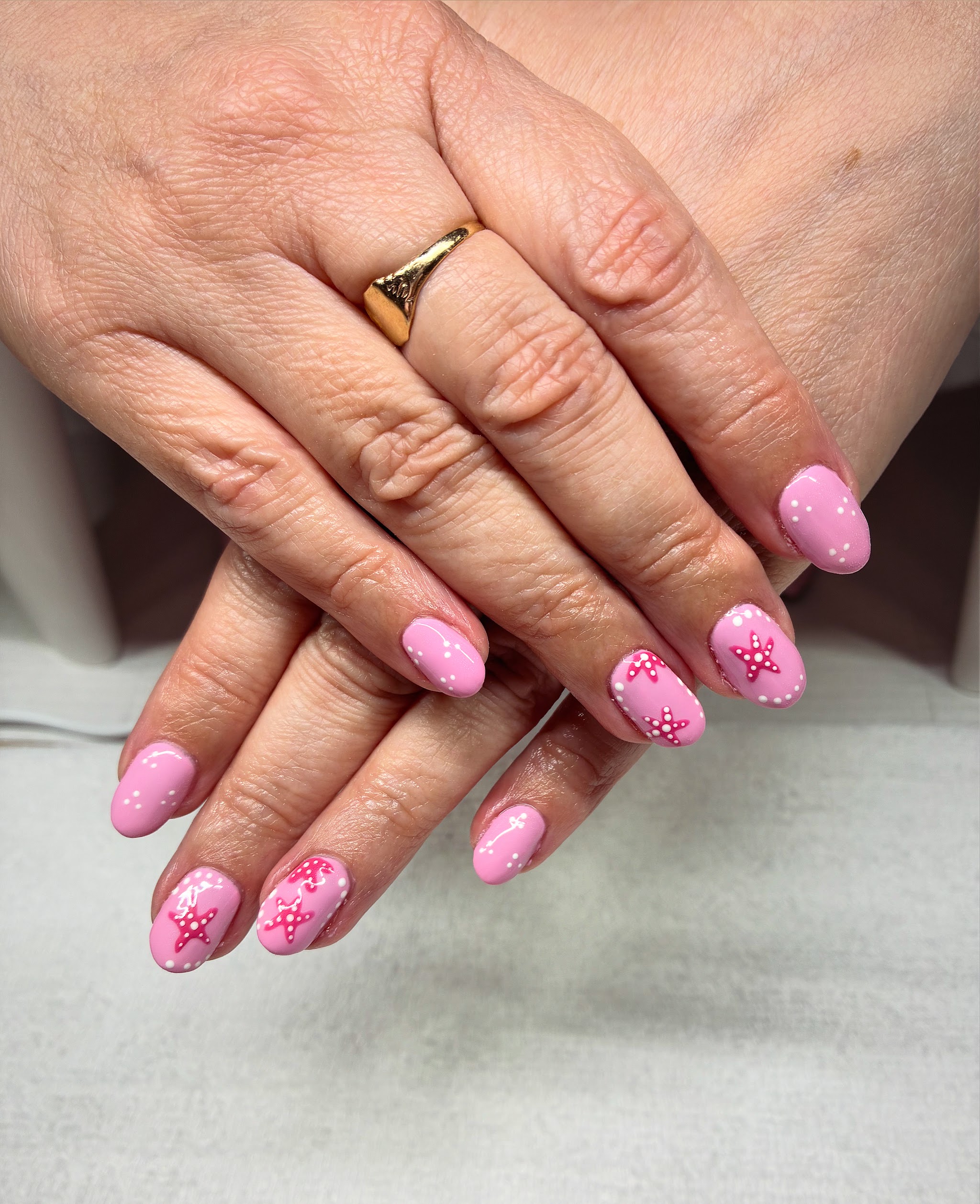 Pink gel nails with floral nail art, hands resting on the white nail lamp