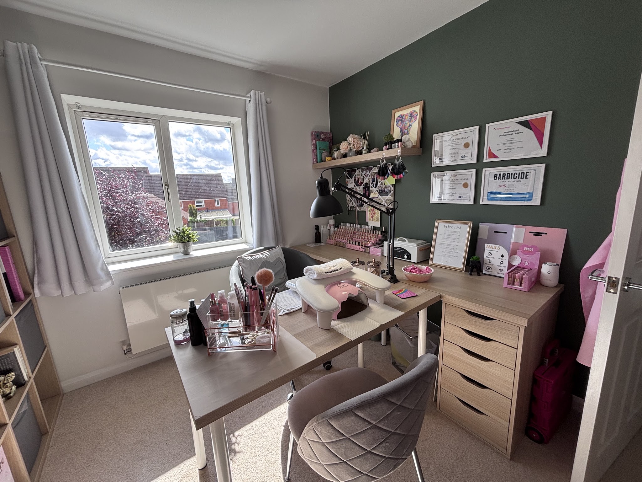 The home salon: a nail desk by the window, a grey chair and framed certificates on a green wall